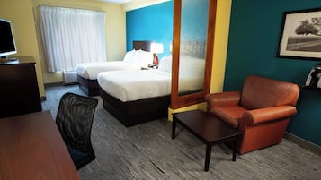 A hotel room with two beds, a desk, a chair, a coffee maker, and a window with curtains.