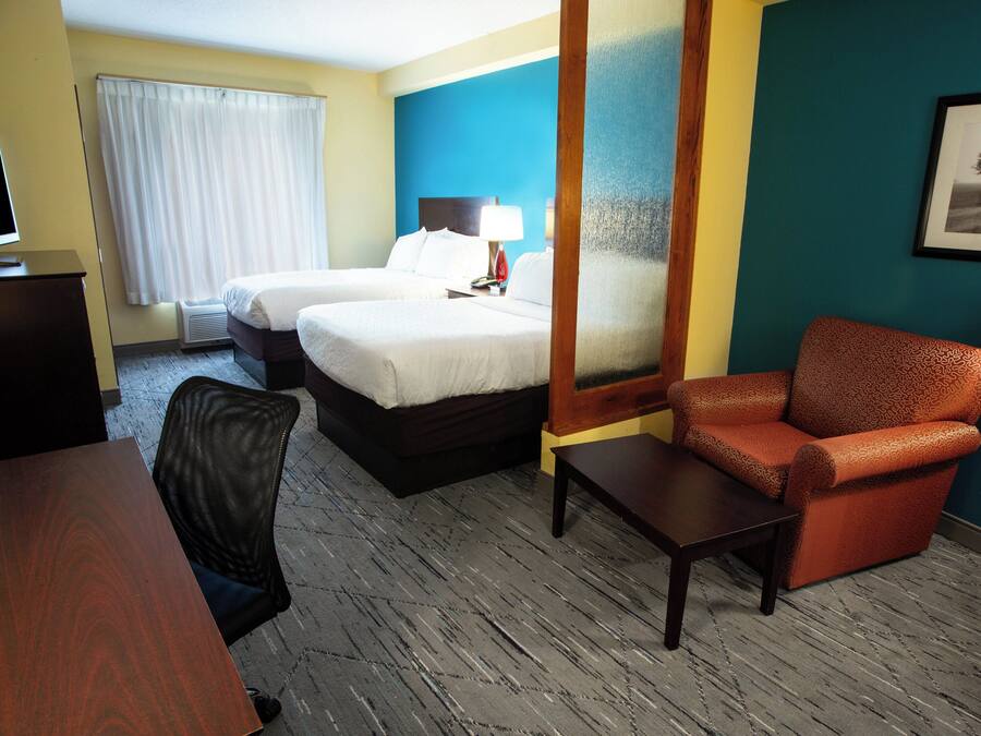 A hotel room with two beds, a desk, a chair, a coffee maker, and a window with curtains.