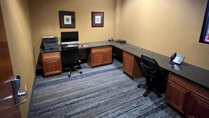 Habitación de hotel con escritorio, silla de oficina y computadora. Se observan cuadros en la pared y piso alfombrado.
