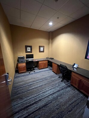 Habitación de hotel con escritorio, silla de oficina y computadora. Se observan cuadros en la pared y piso alfombrado.