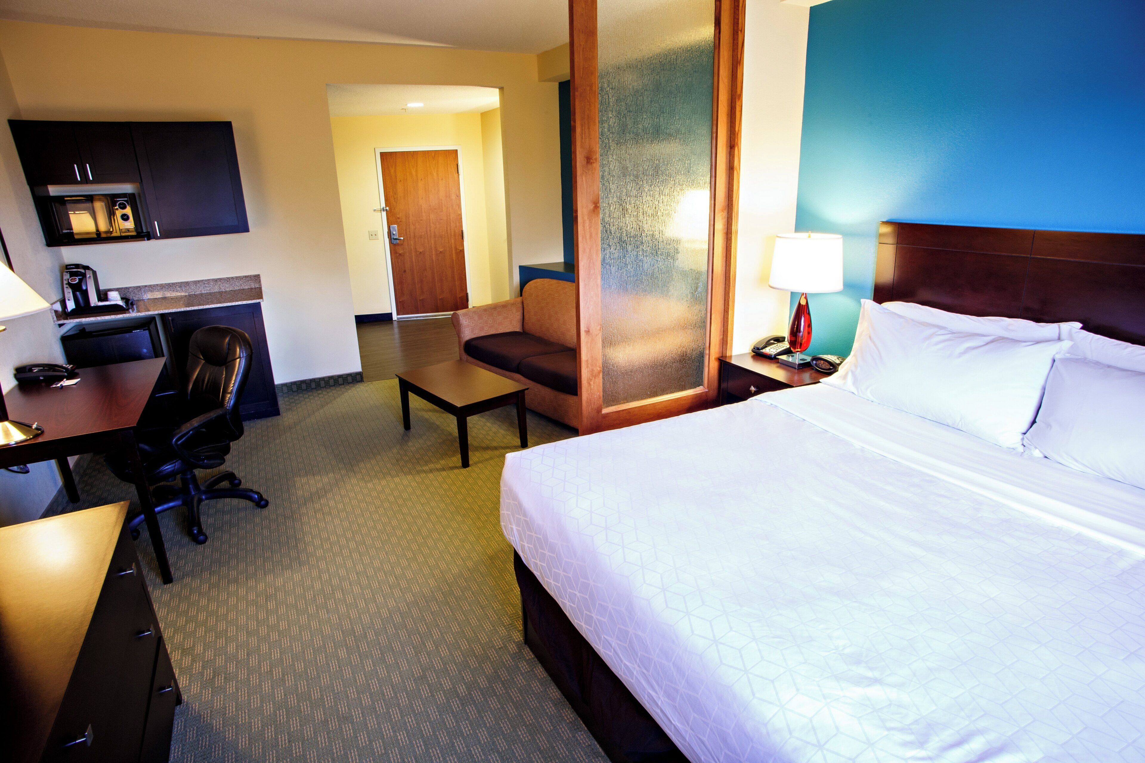 Une chambre d’hôtel comprenant un lit, un bureau, une chaise, une table de chevet avec une lampe et une porte donnant sur une autre pièce.