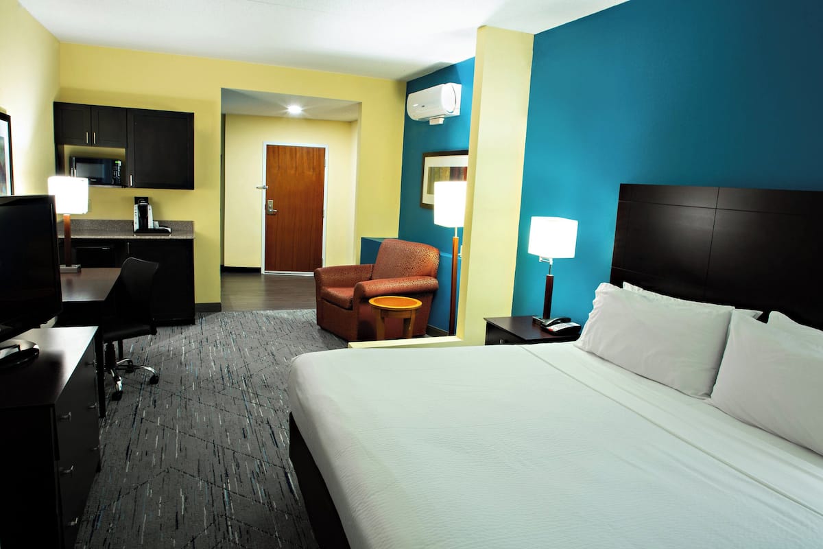 A hotel room with a bed, desk, chair, and kitchenette.