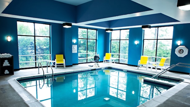 Una piscina con agua azul cristalina, rodeada de muros azules y grandes ventanales.