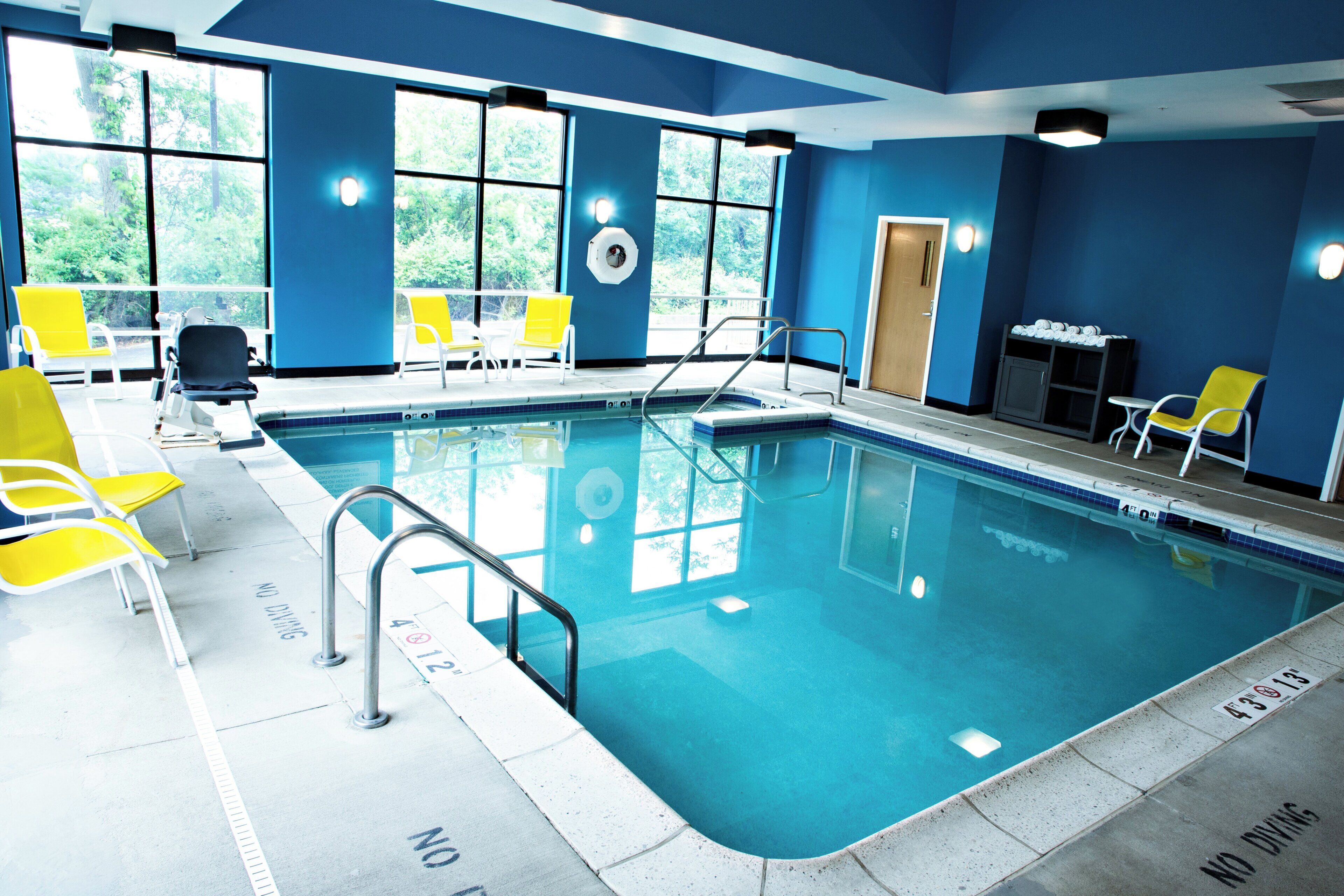 Una piscina interior con agua cristalina, sillas amarillas y un cartel que indica 'no buceo' junto a la piscina.