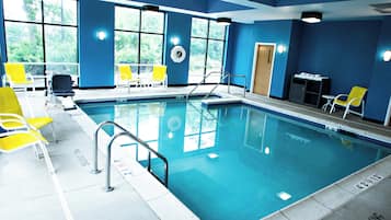 Piscina interna com água cristalina, cadeiras amarelas e placa de proibição de mergulho na borda da piscina.
