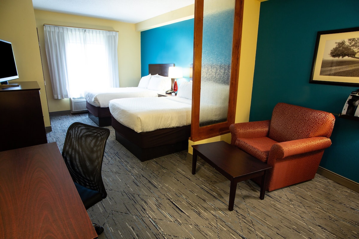 A hotel room with two beds, a desk, a chair, a TV, and a framed picture on the wall.