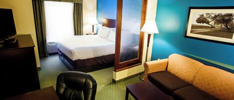 A hotel room with a bed, a desk, a leather chair, a sofa, and a painting on the wall.