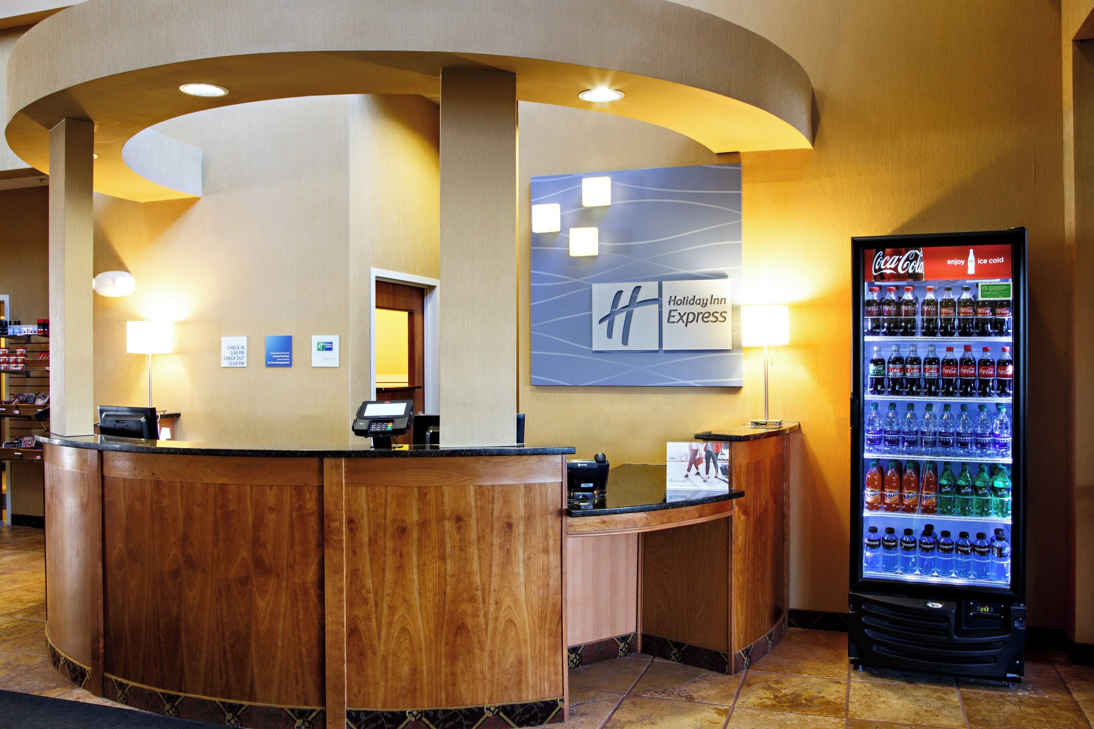 A hotel reception area with a check-in counter, a Coca-Cola refrigerator, and a Holiday Inn Express sign.
