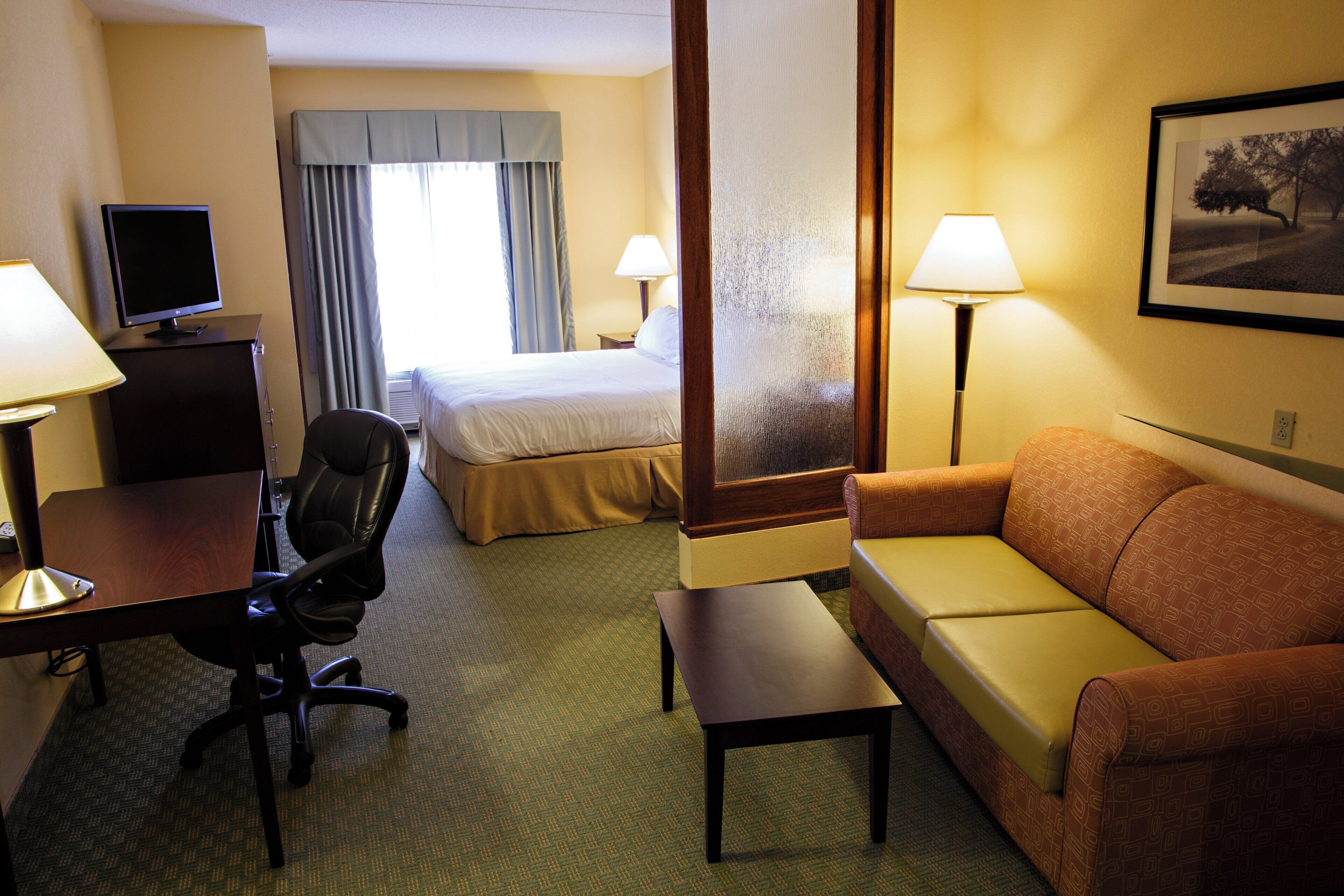 Een hotelkamer met een bed, een bureau met een computer, een stoel, een bank, twee lampen en een lijst aan de muur.