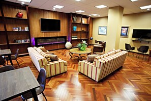 A hotel lobby with a seating area, a television, and a bookshelf.