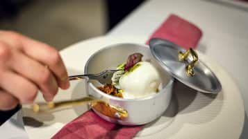 A dessert in a white bowl with a lid, a spoon, and a napkin on a table.