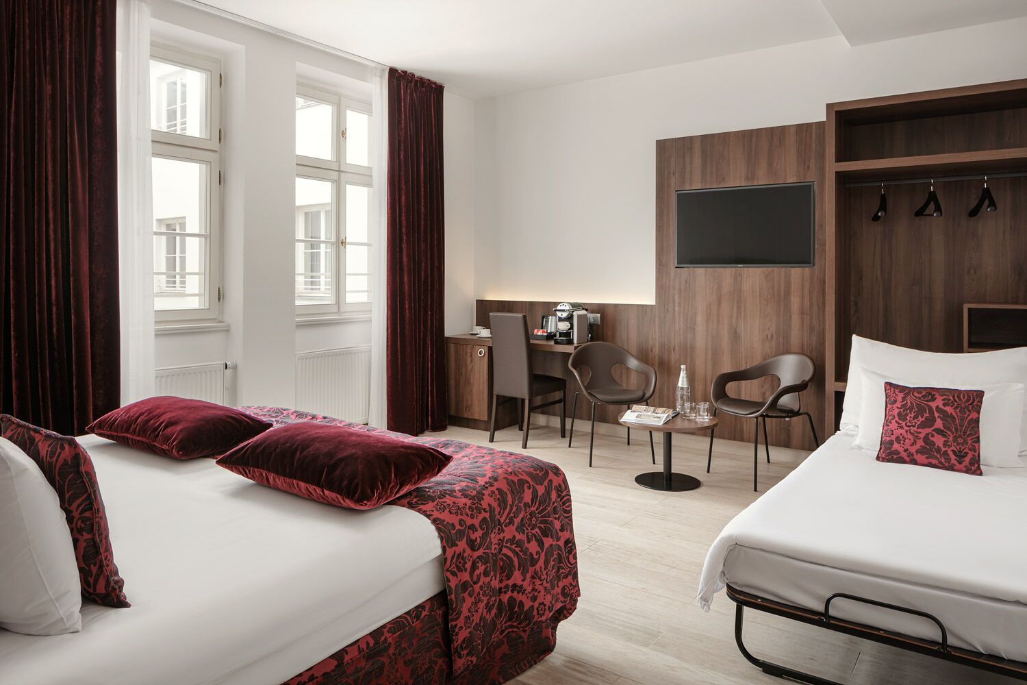 Una habitación de hotel con dos camas, un escritorio, sillas, un televisor y un perchero.