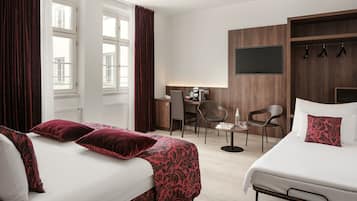 A hotel room with two beds, a desk, chairs, a TV, and a coat rack.