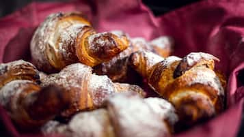 Uma cesta com doces, incluindo croissants e um éclair de chocolate, polvilhada com açúcar em pó.