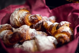 Uma cesta com doces, incluindo croissants e um éclair de chocolate, polvilhada com açúcar em pó.