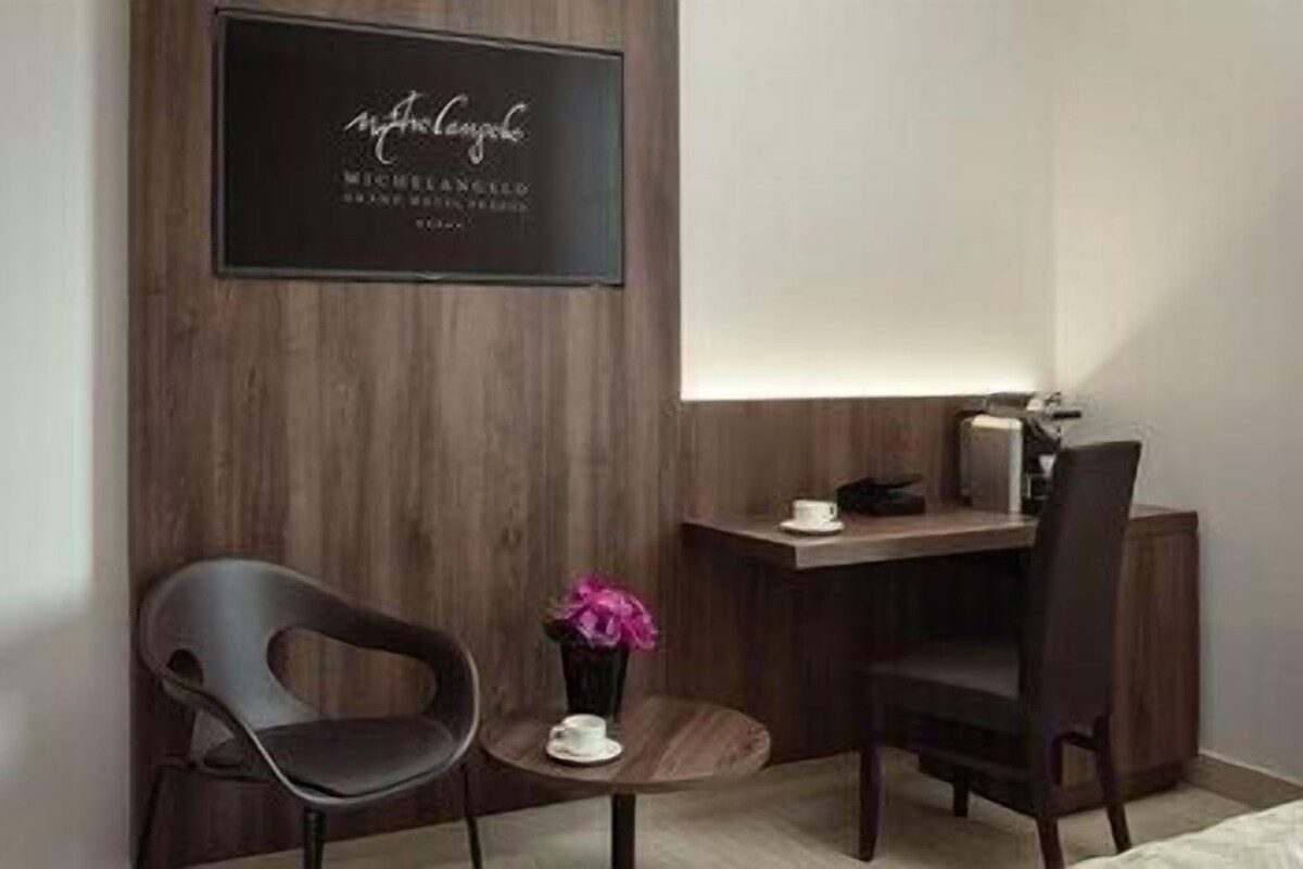 A modern room with a wooden wall, a small round table with a cup and flower, two chairs, and a desk with a lamp.