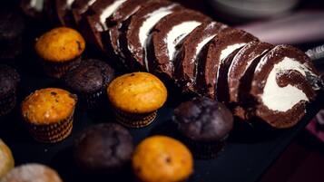 Un postre de chocolate con remolinos de crema blanca, rodeado de diversos cupcakes y muffins.
