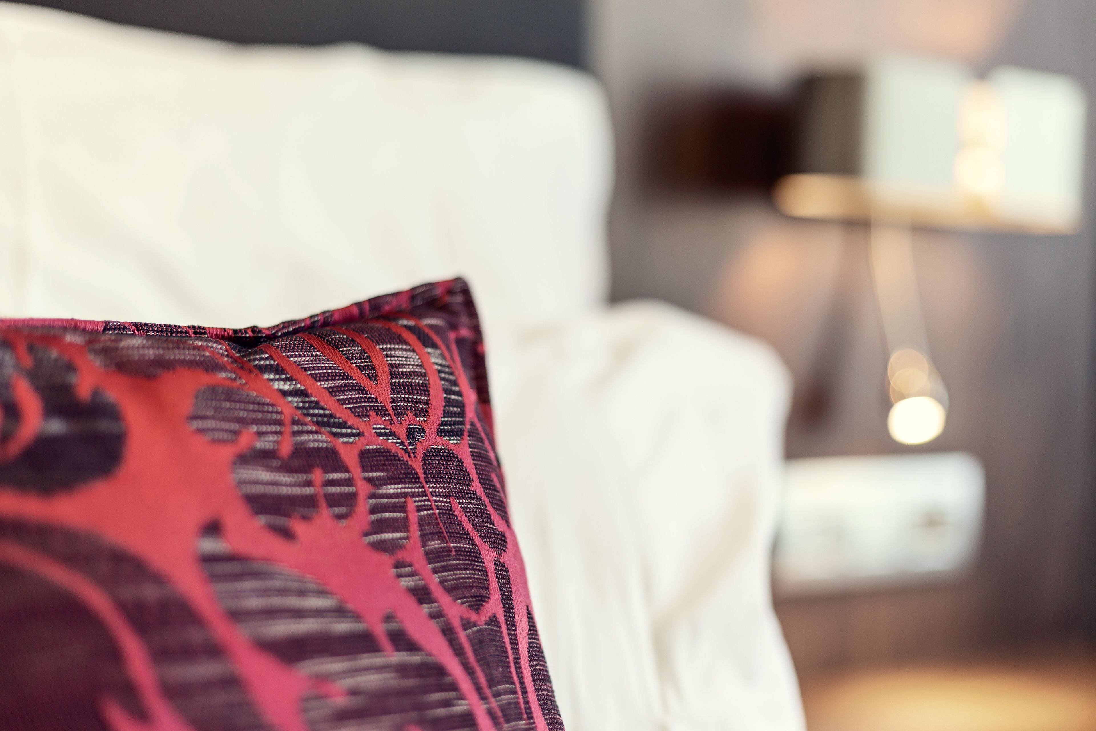 Um close-up de uma cama com colchão branco e almofada vermelha estampada.