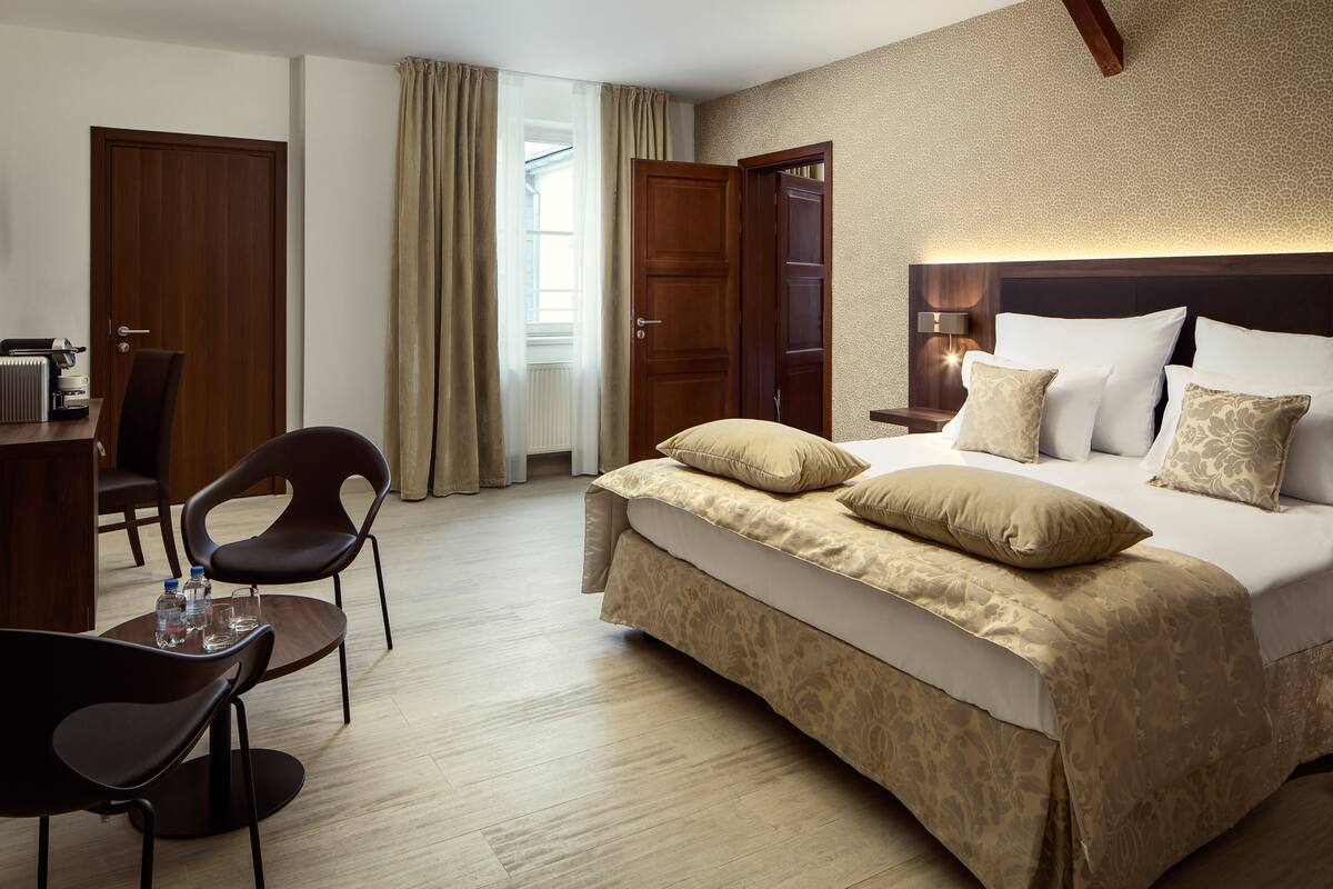 Una habitación de hotel con una cama grande, un escritorio con una silla, un radiador y una ventana con cortinas.