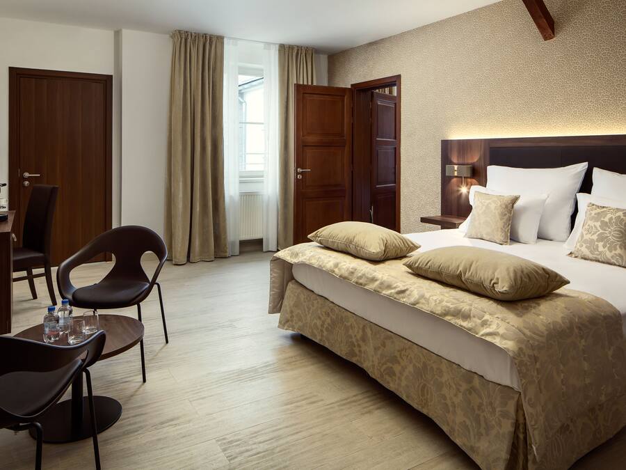 A hotel room with a large bed, a desk with a chair, a radiator, and a window with curtains.
