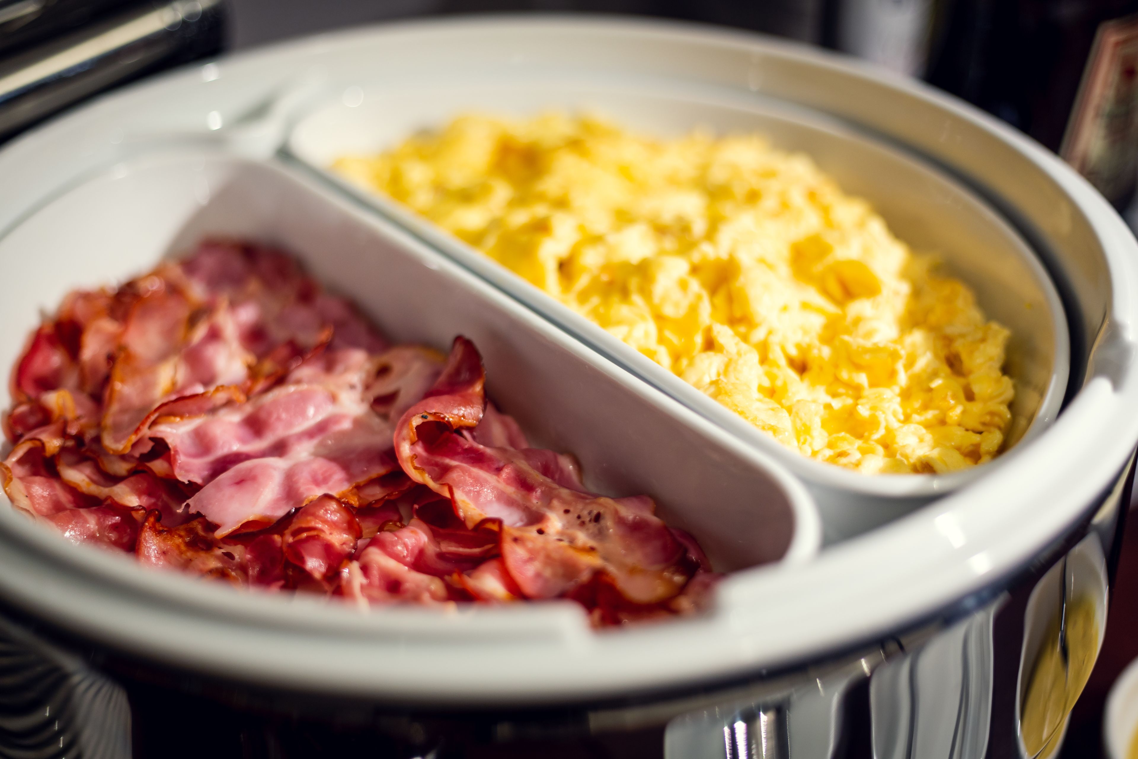 A breakfast tray with scrambled eggs and bacon.