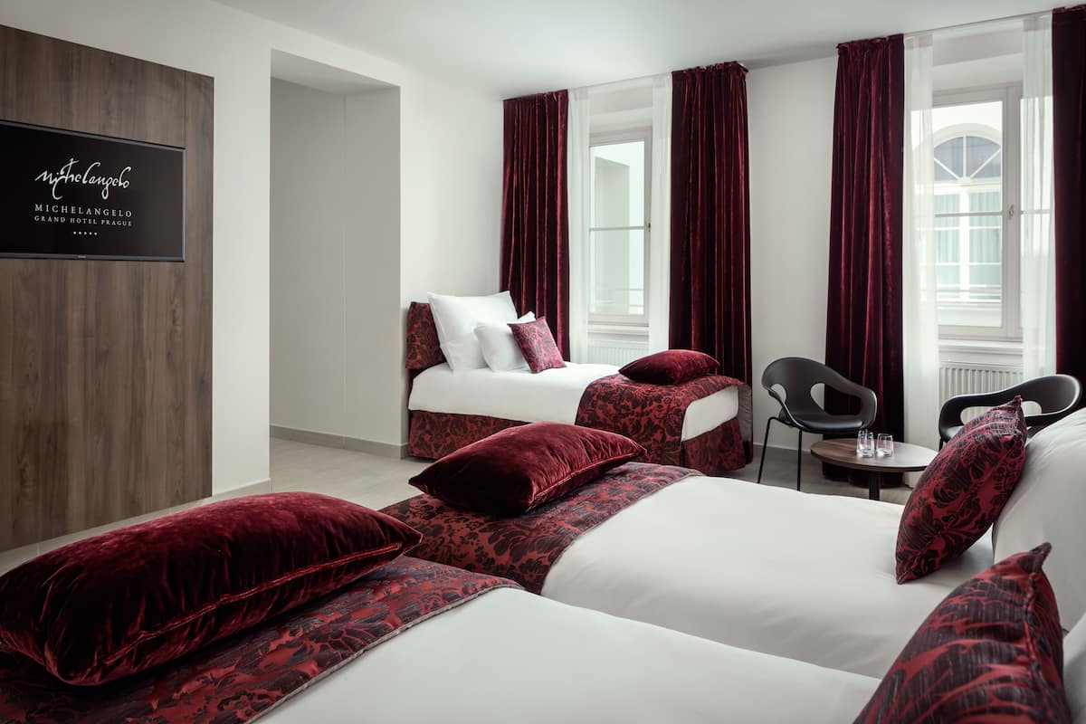 Habitación de hotel con dos camas, ropa de cama roja y blanca, un revestimiento de pared de madera, un televisor y vistas a la calle.