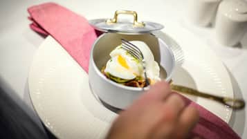 Un tazón blanco con tapa sobre un plato blanco, un tenedor y una servilleta rosa.