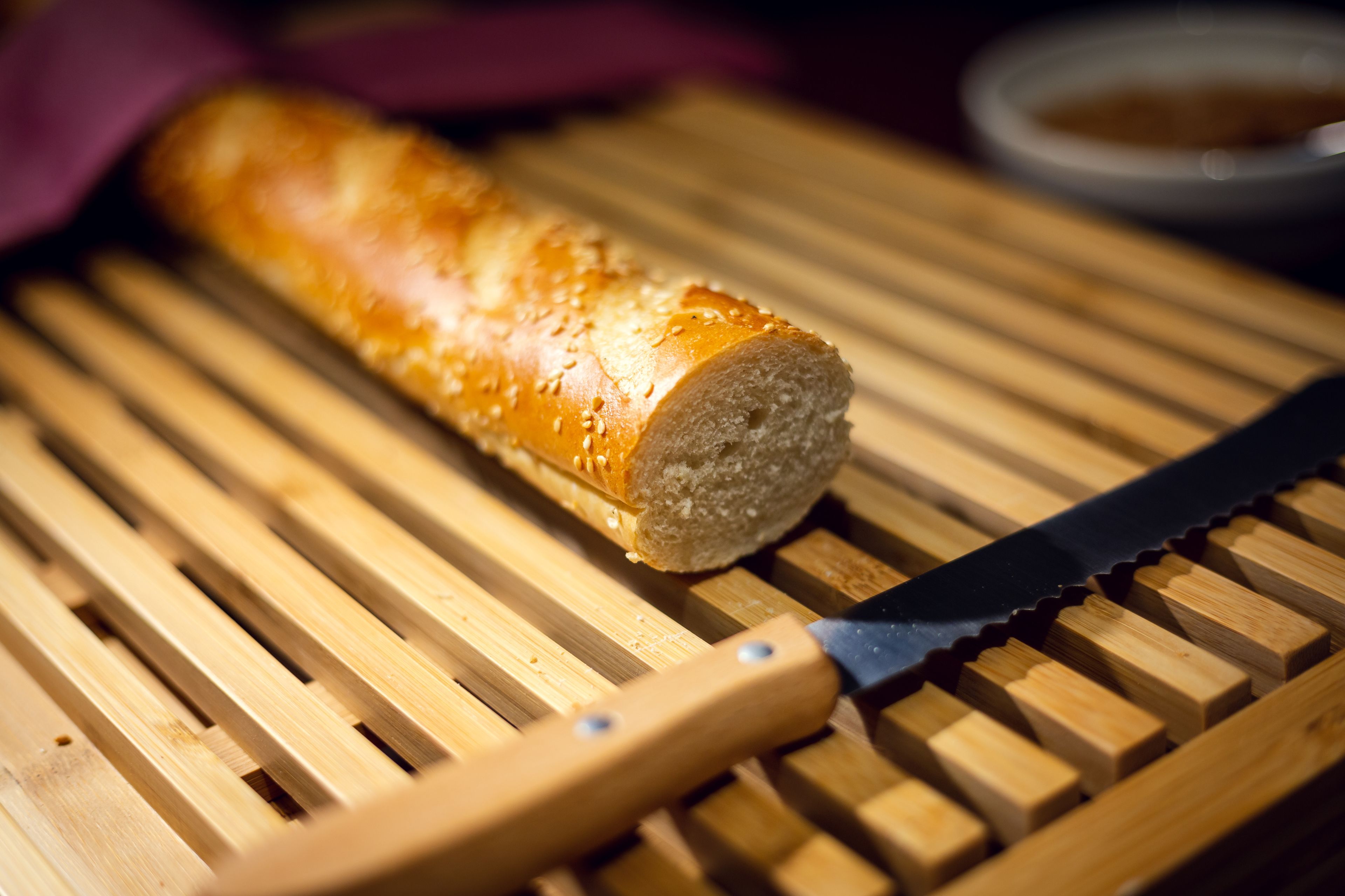 A baguette on a wooden cutting board with a knife beside it.