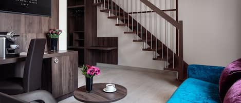 Una habitación de hotel moderna con una escalera de madera, un sofá azul, un comedor con mesa y sillas, y una cafetera.
