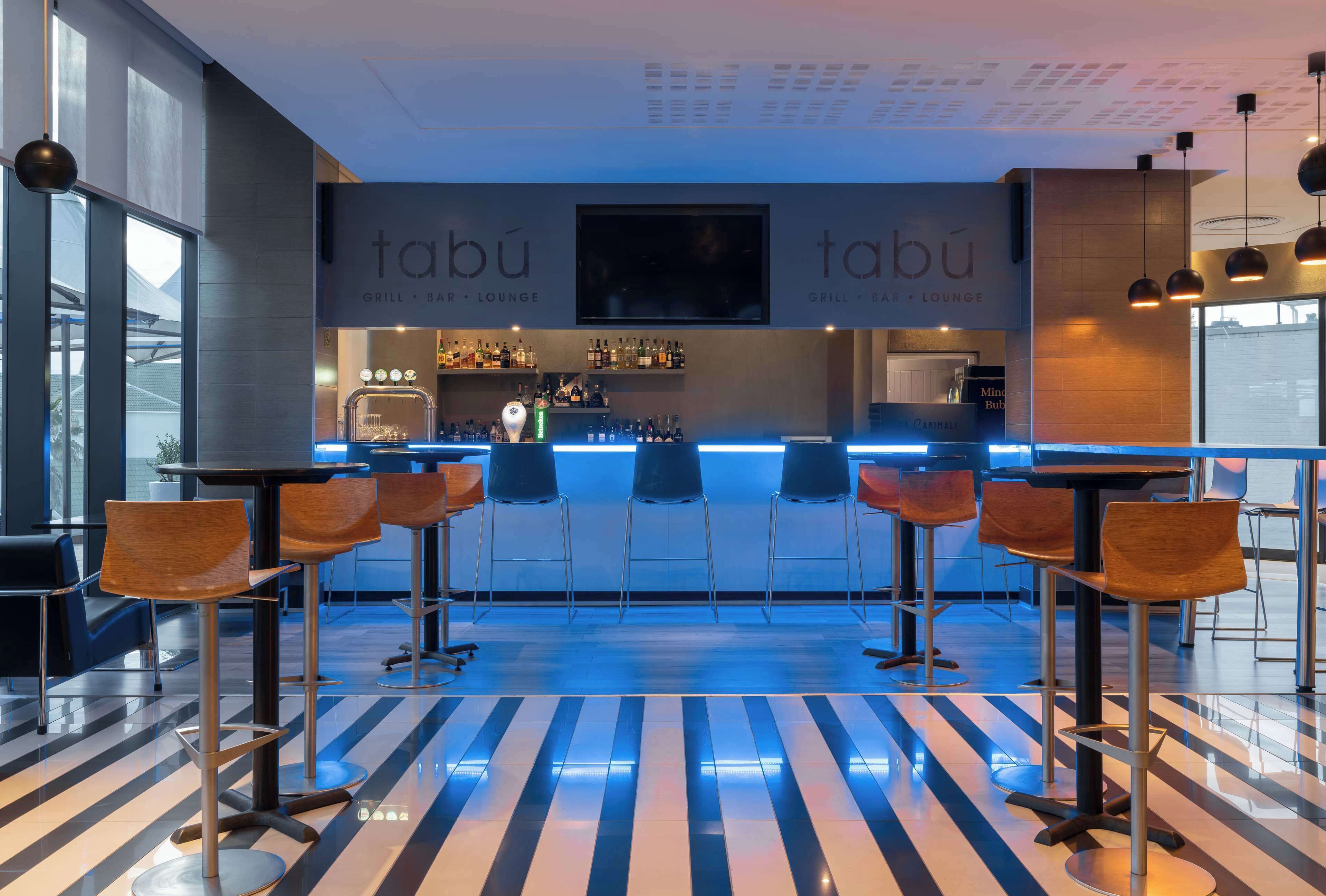 A modern bar area with a striped floor, bar stools, and a counter with a menu.
