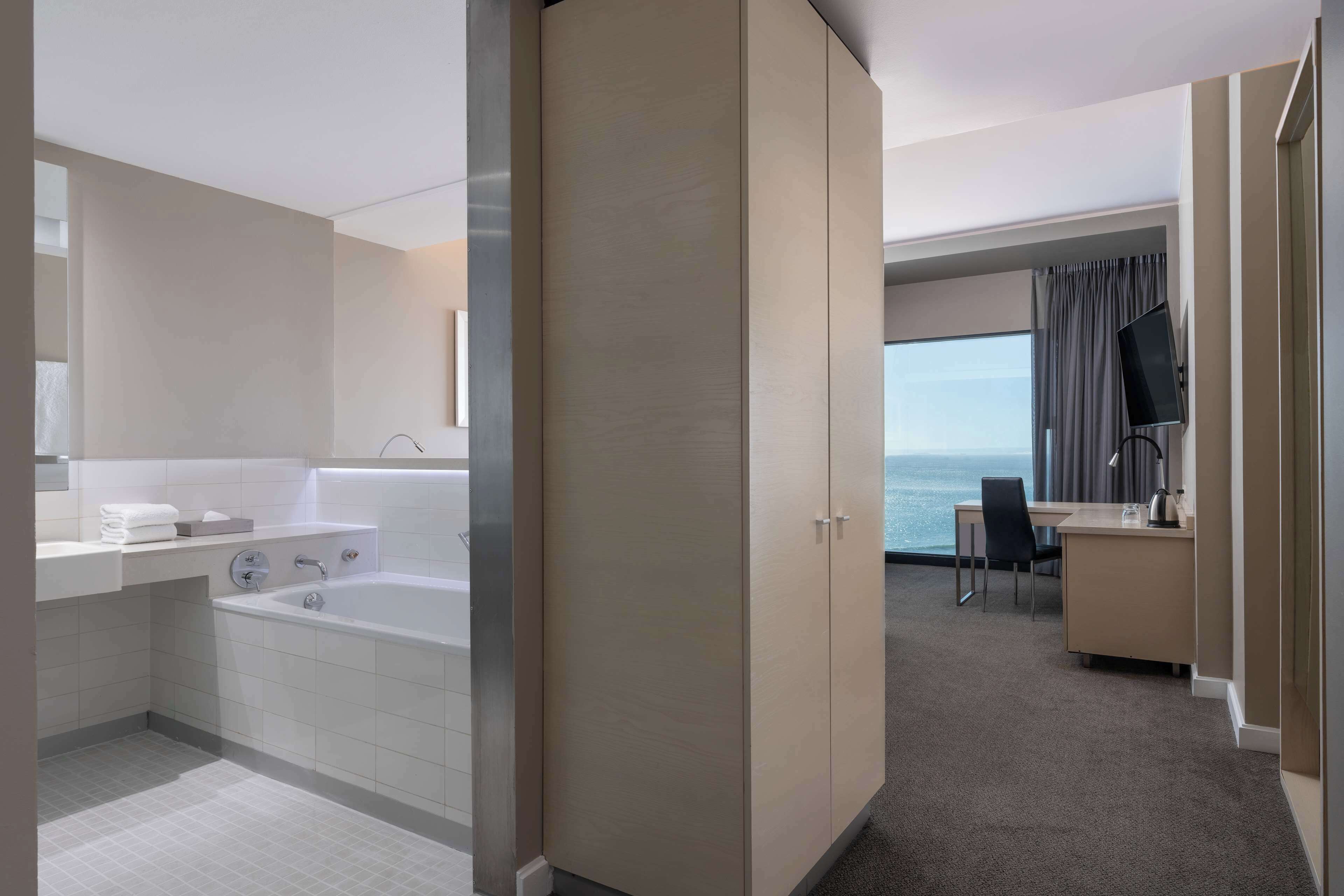 A modern hotel room with a bathtub, a desk, and a view of the sea.
