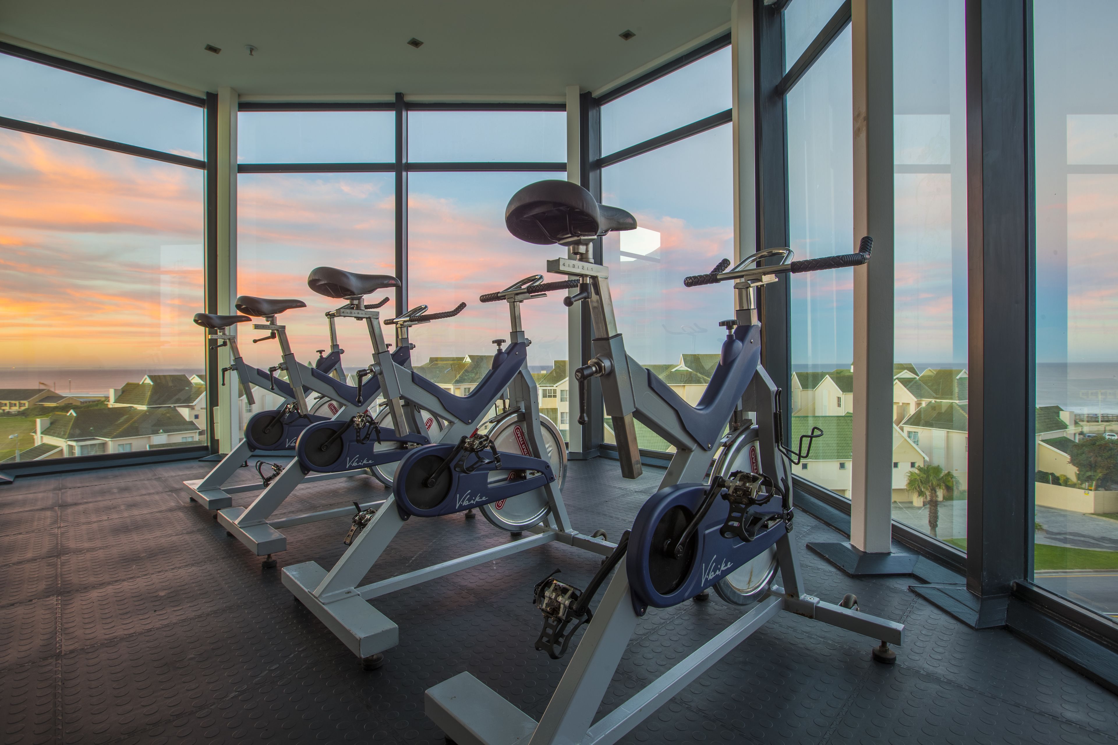 Ett gym med motionscyklar och stora fönster med utsikt över ett bostadsområde.