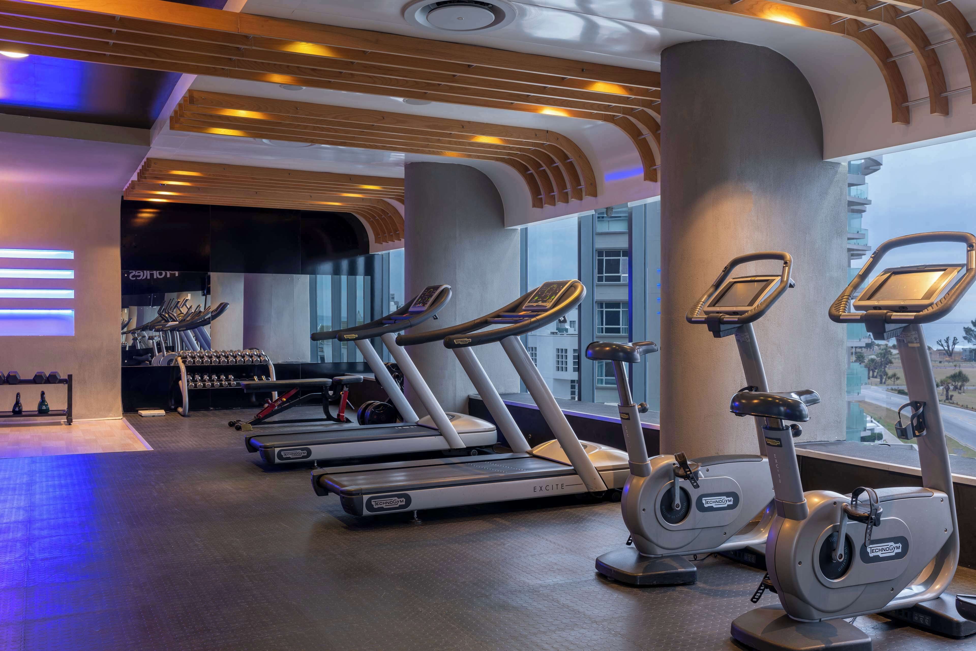 A gym with treadmills and elliptical machines, large windows, and a view of the city.