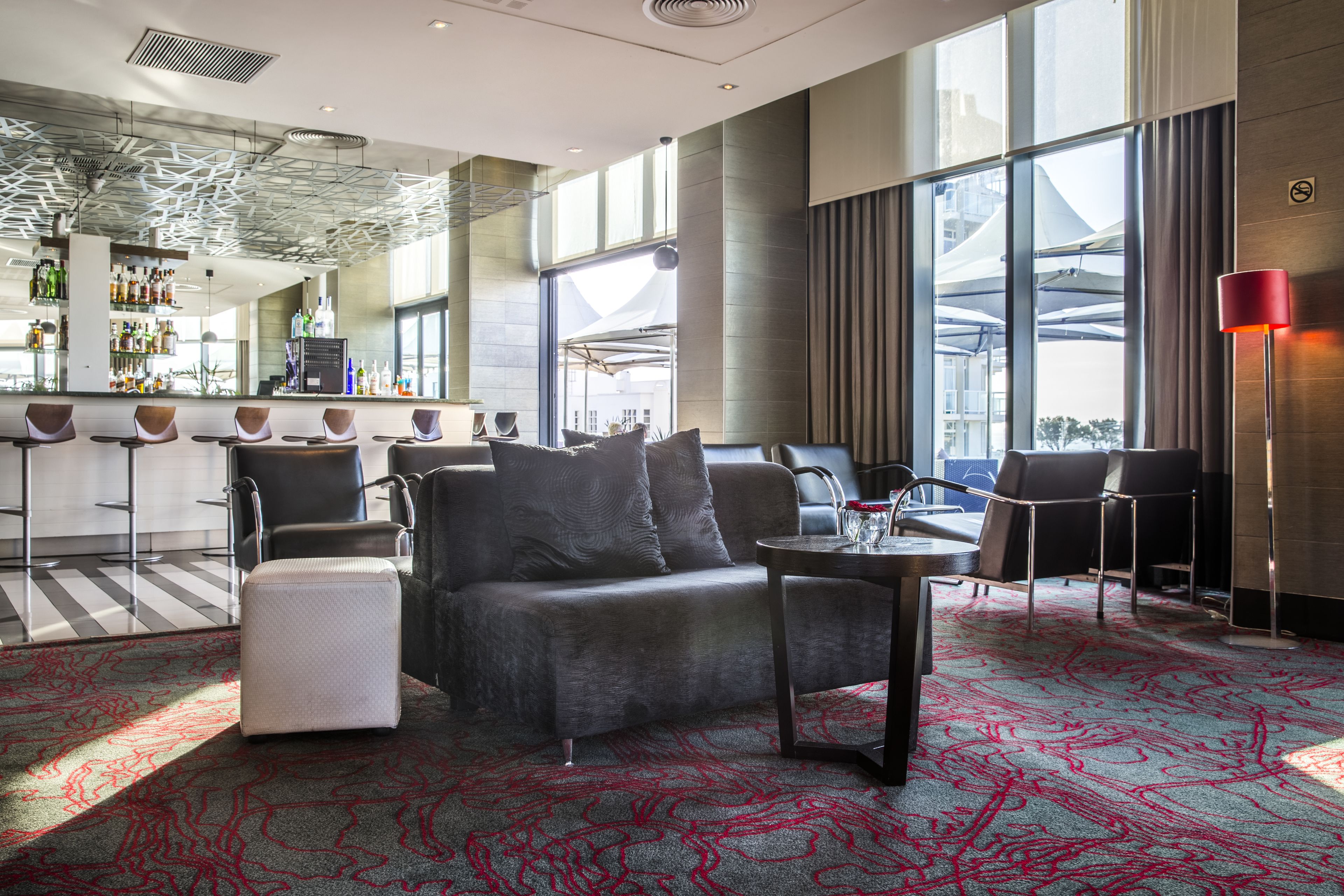 A modern hotel lobby with a bar area, seating, and large windows.