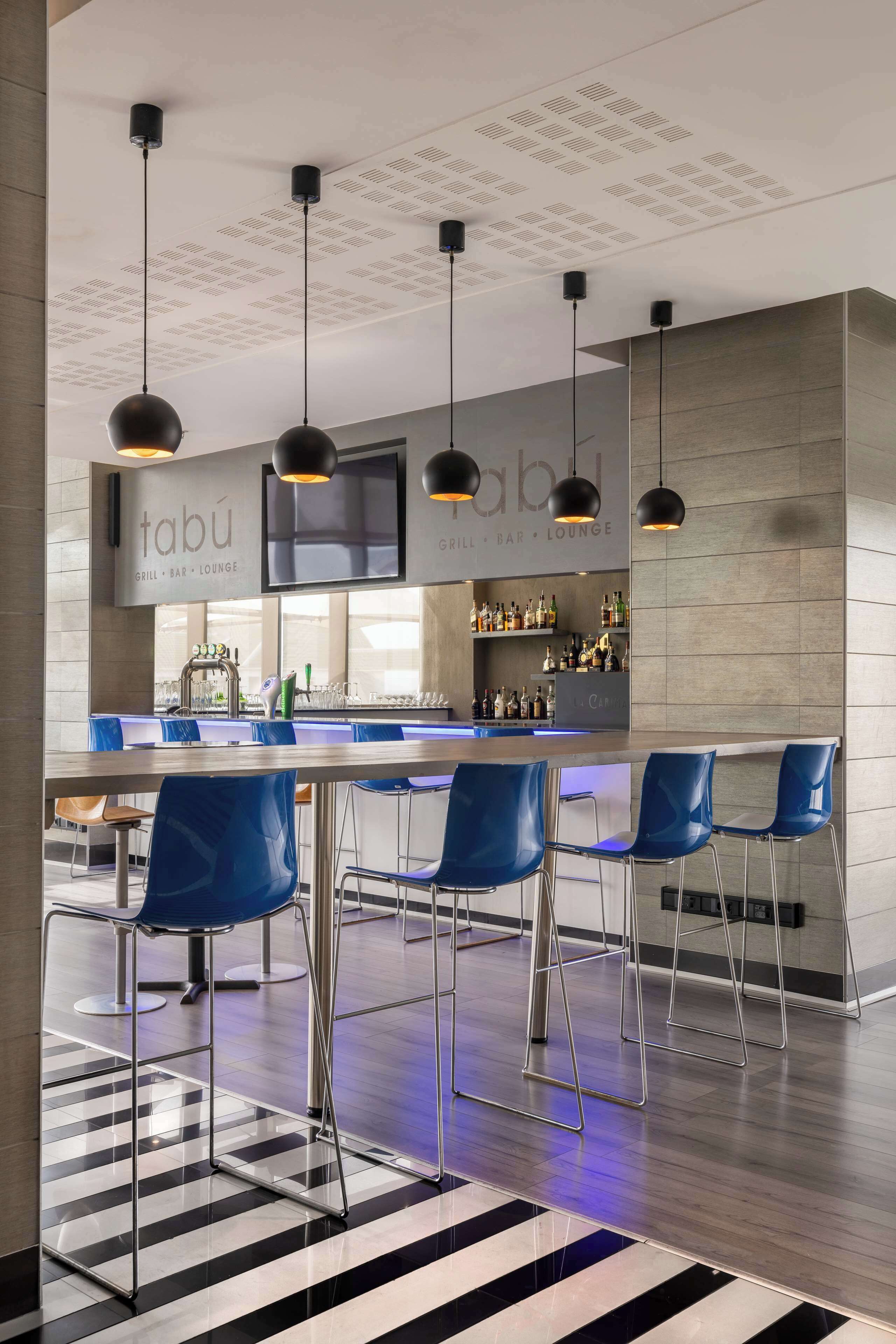 A modern bar area with blue bar stools, a counter with a barista machine, and a ceiling with recessed lighting.