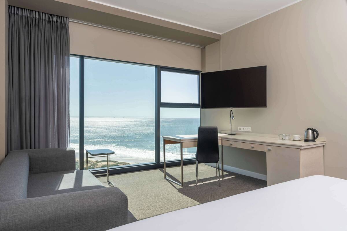Ein Hotelzimmer mit großem Fenster und Meerblick, ein Bett, ein Schreibtisch mit Stuhl und ein Flachbildfernseher.