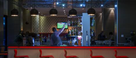 A bar area with a bartender, red bar stools, and a television screen.
