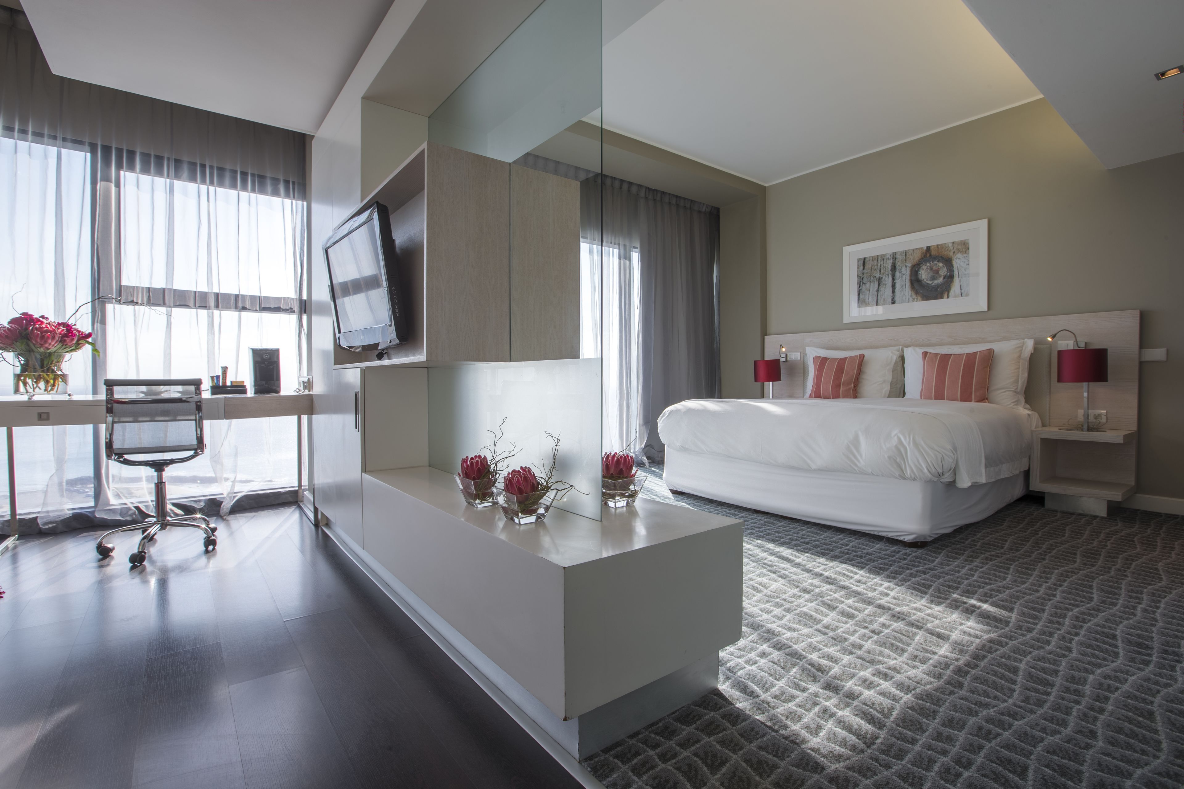 A modern hotel room with a bed, a desk, a chair, a TV, and a large mirror.