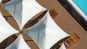 Un espace aménagé au bord de la piscine, avec des parasols blancs et des chaises longues en bois.