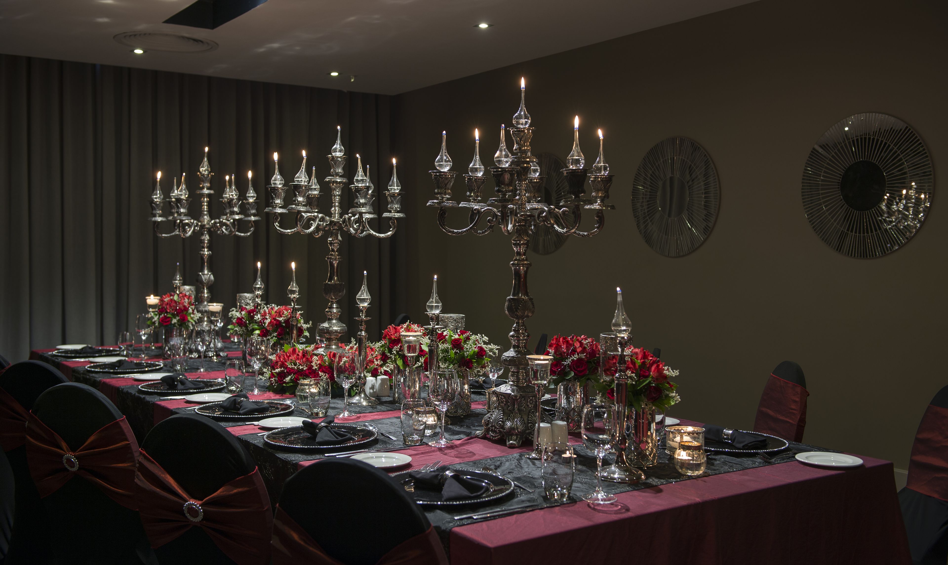 A formal dining room with a long table set for a meal, surrounded by chairs with red bows.