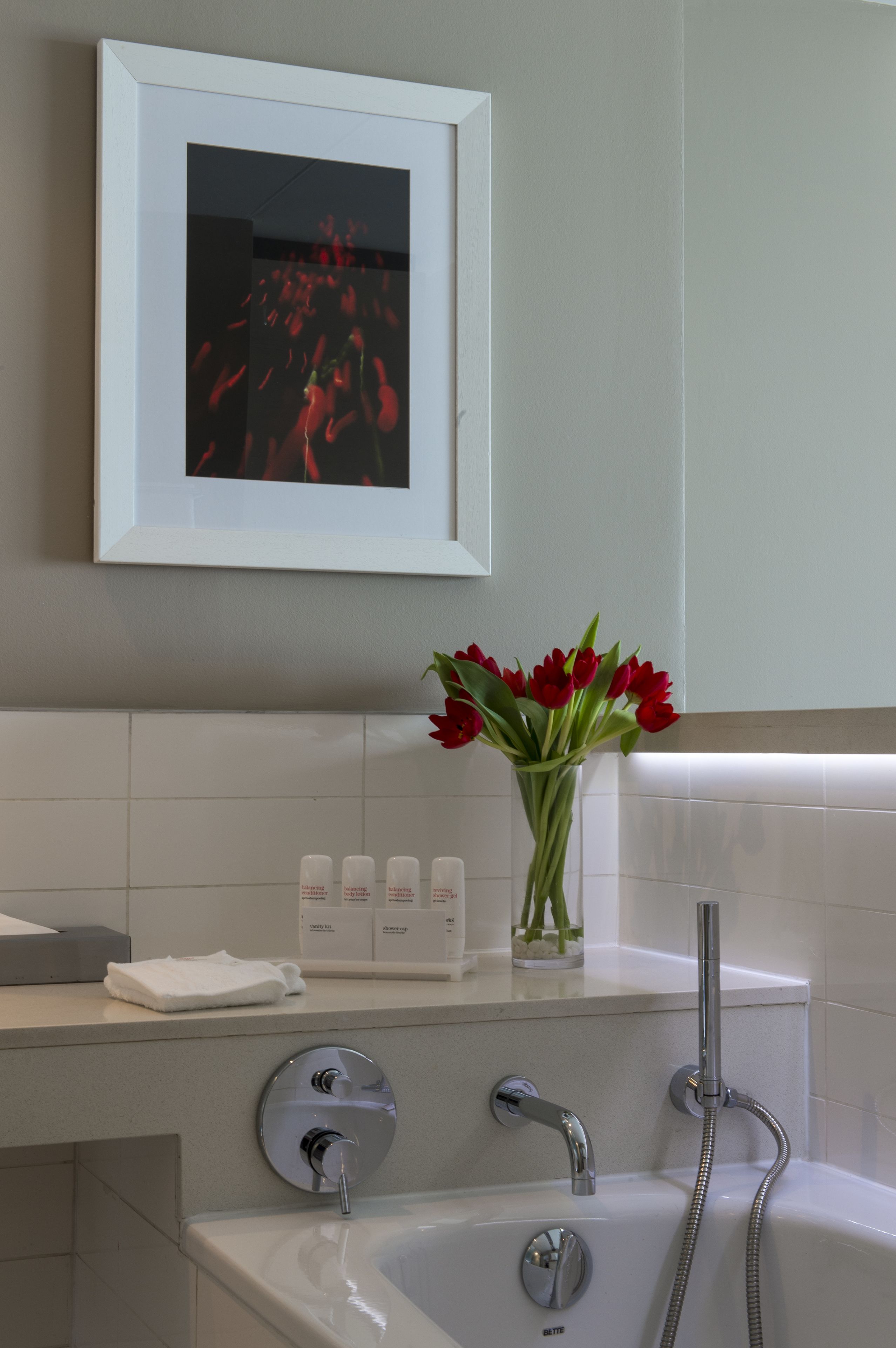 A bathroom with a white sink, a framed picture above it, and a vase with red flowers on the counter.