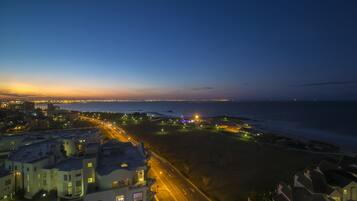 A coastal cityscape at dusk with illuminated streets and buildings.