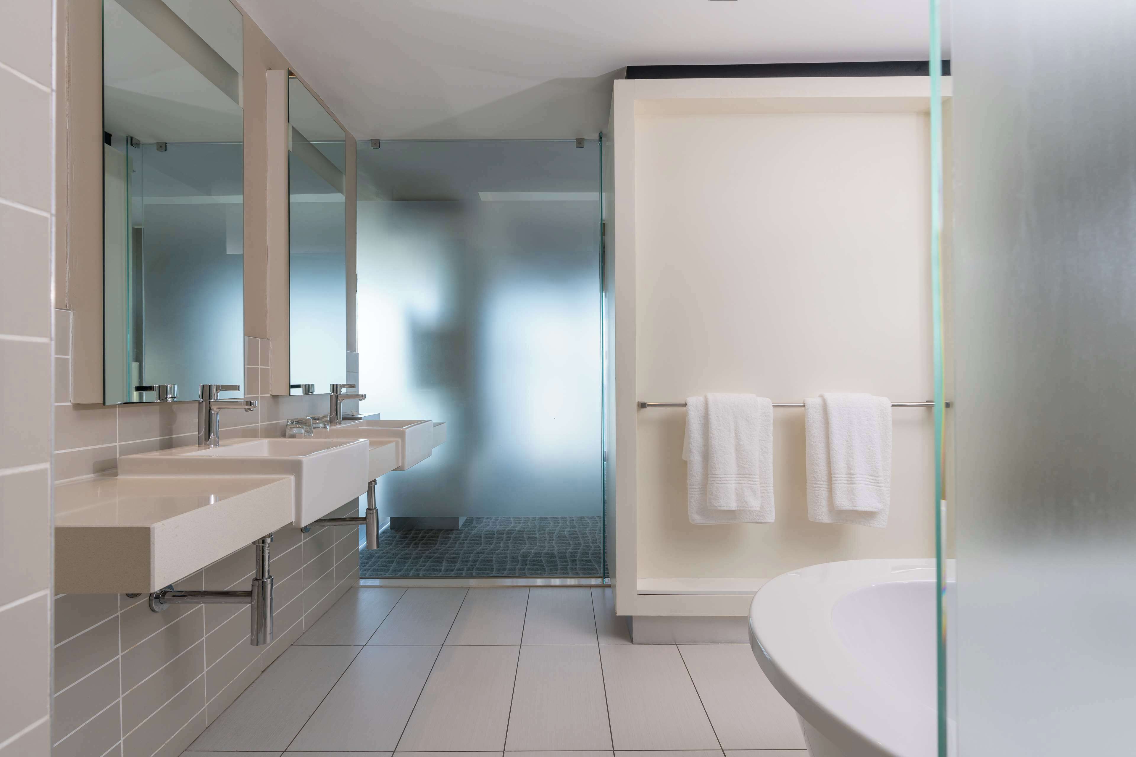 A modern bathroom with two sinks, a bathtub, and a glass shower enclosure.
