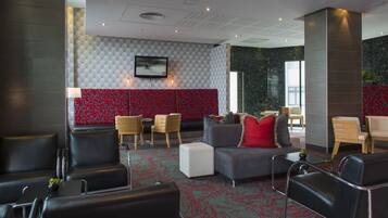 Een moderne lobby met lederen zitplaatsen, een kamerbreed tapijt en een combinatie van rode en grijze decoratie.
