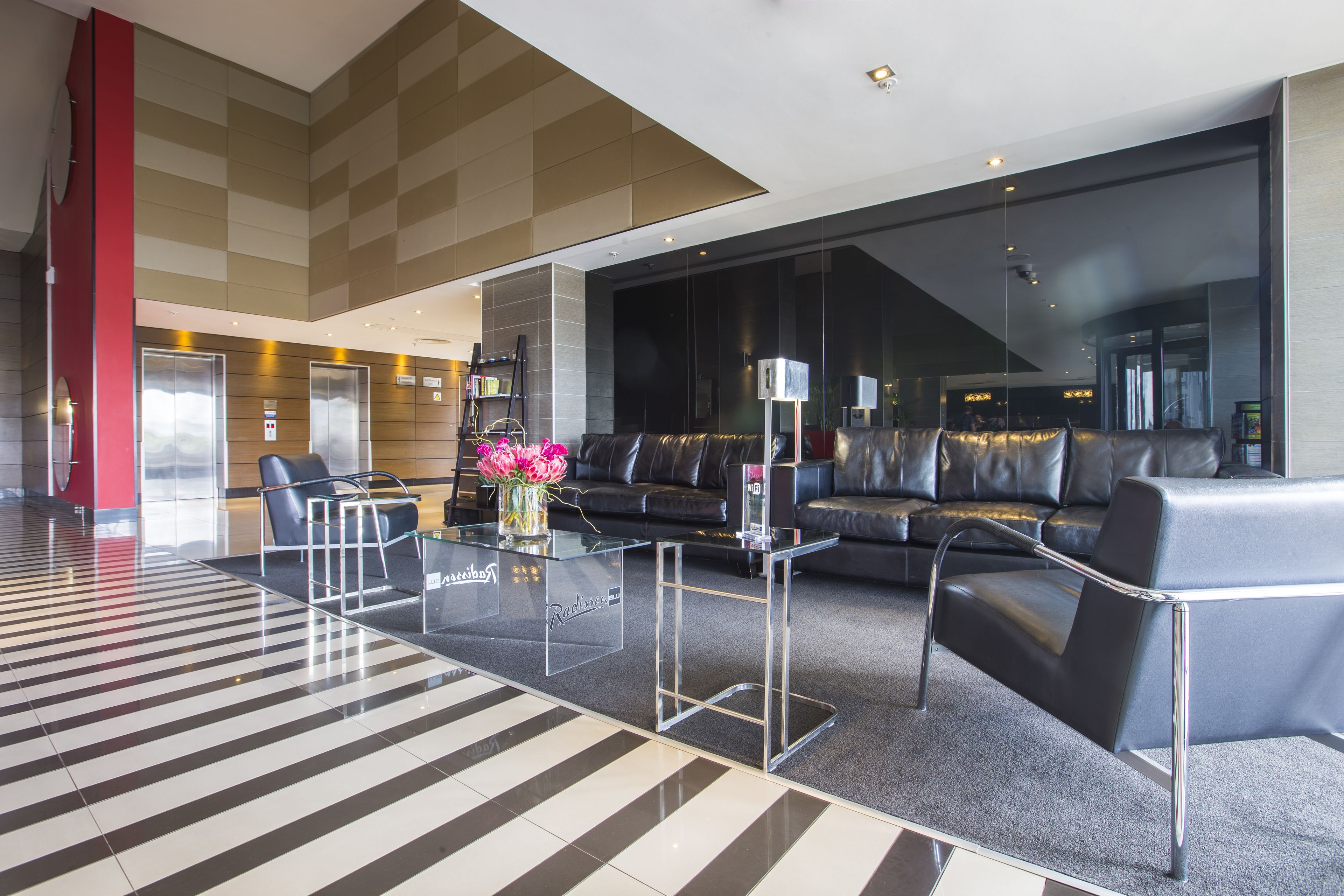 A modern lobby with a glass coffee table, leather sofas, and a striped floor.