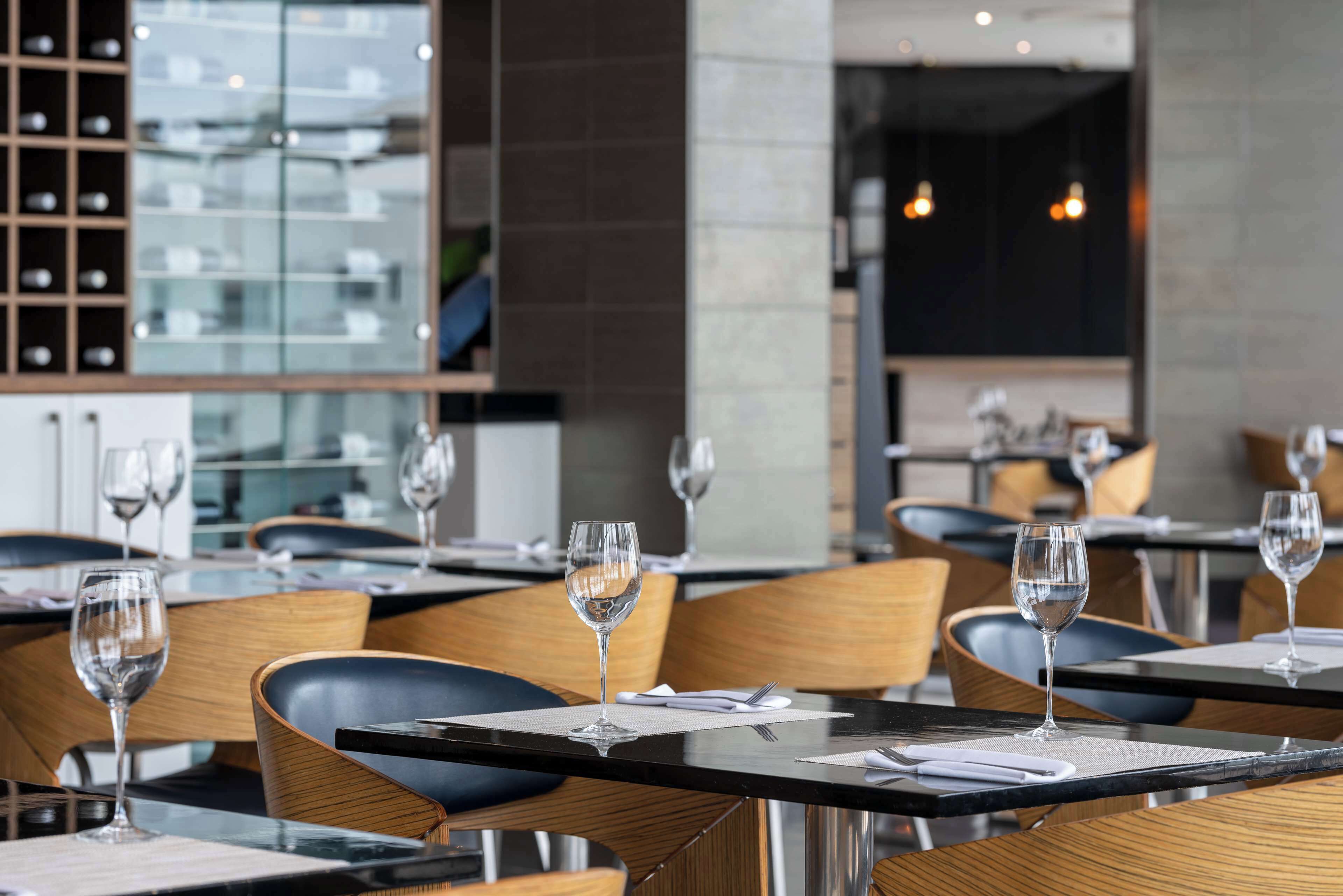 A restaurant interior with tables set for dining, wine glasses, and a wine rack in the background.