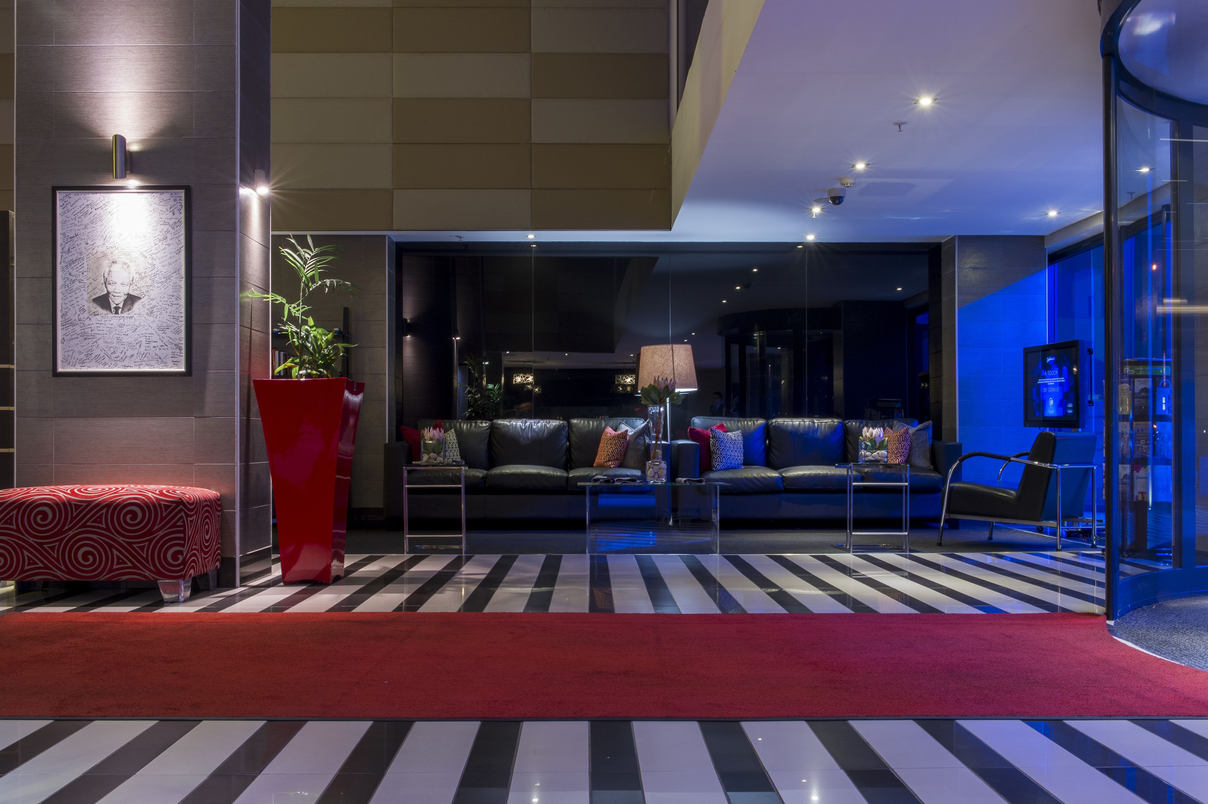 Un hall d’hôtel moderne avec un sol à rayures, un banc rouge, un ensemble de canapés et une grande plante en pot.