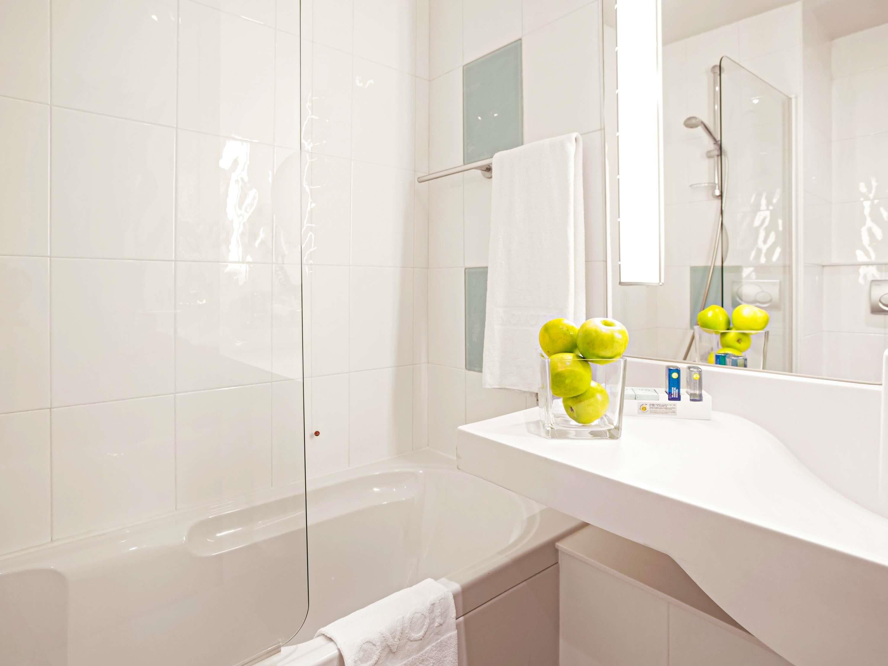 A modern bathroom with a white vanity, a glass vase with green apples, and a large mirror.
