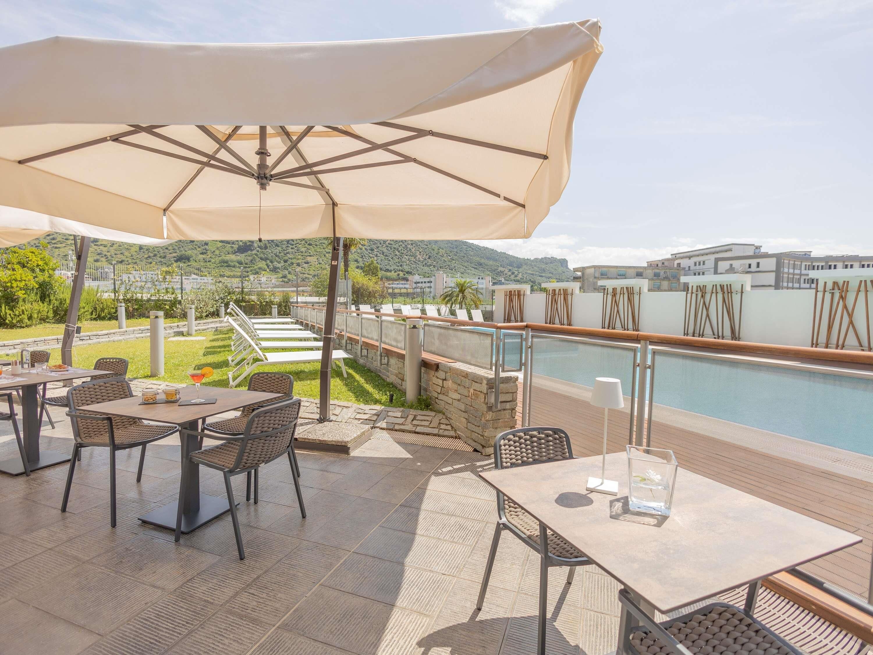 An outdoor patio with tables and chairs, a swimming pool, and a view of the surrounding landscape.