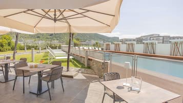 Une terrasse extérieure avec des tables et des chaises, une piscine et une vue sur le paysage environnant.